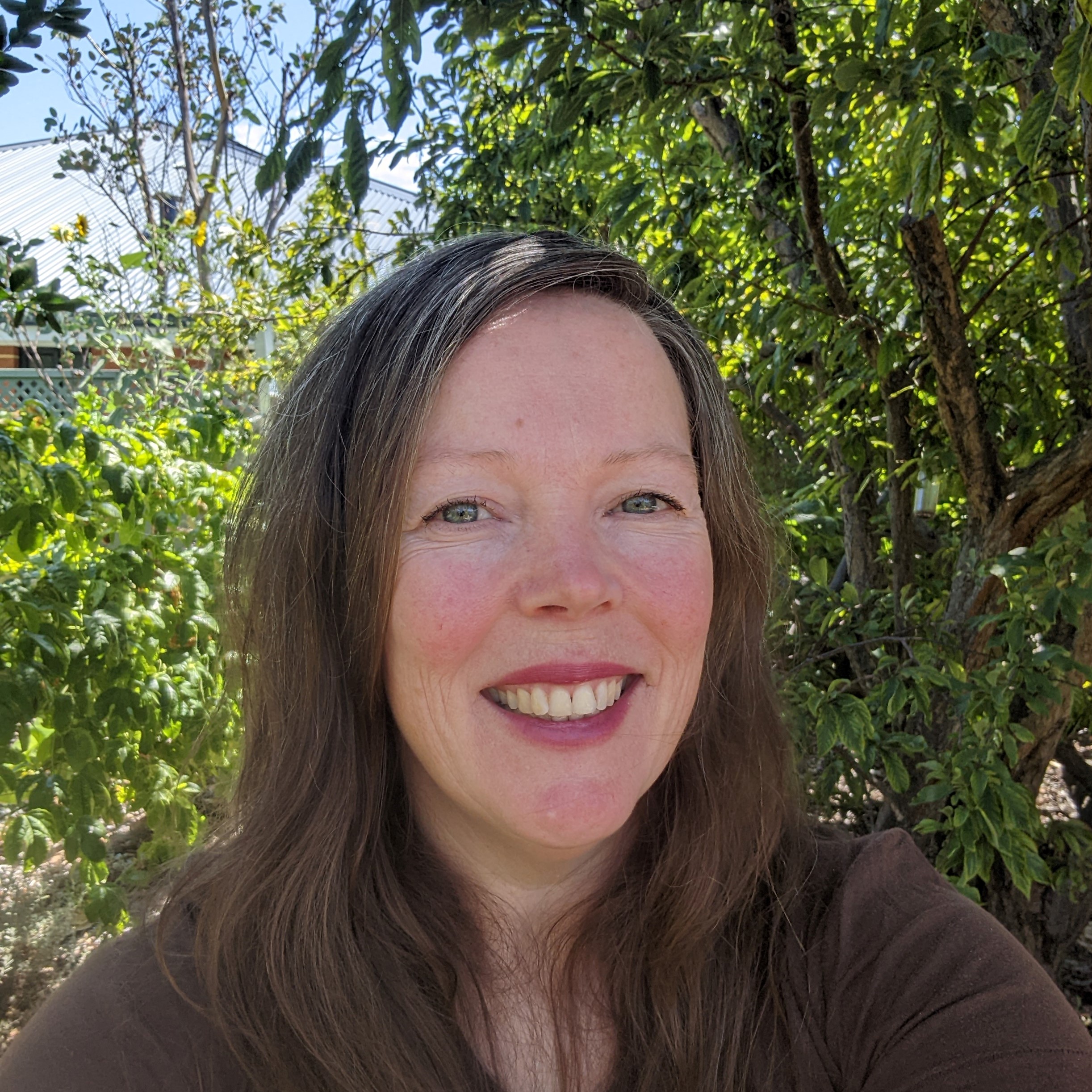 Woman smiling taking photo of herself with green trees in the background