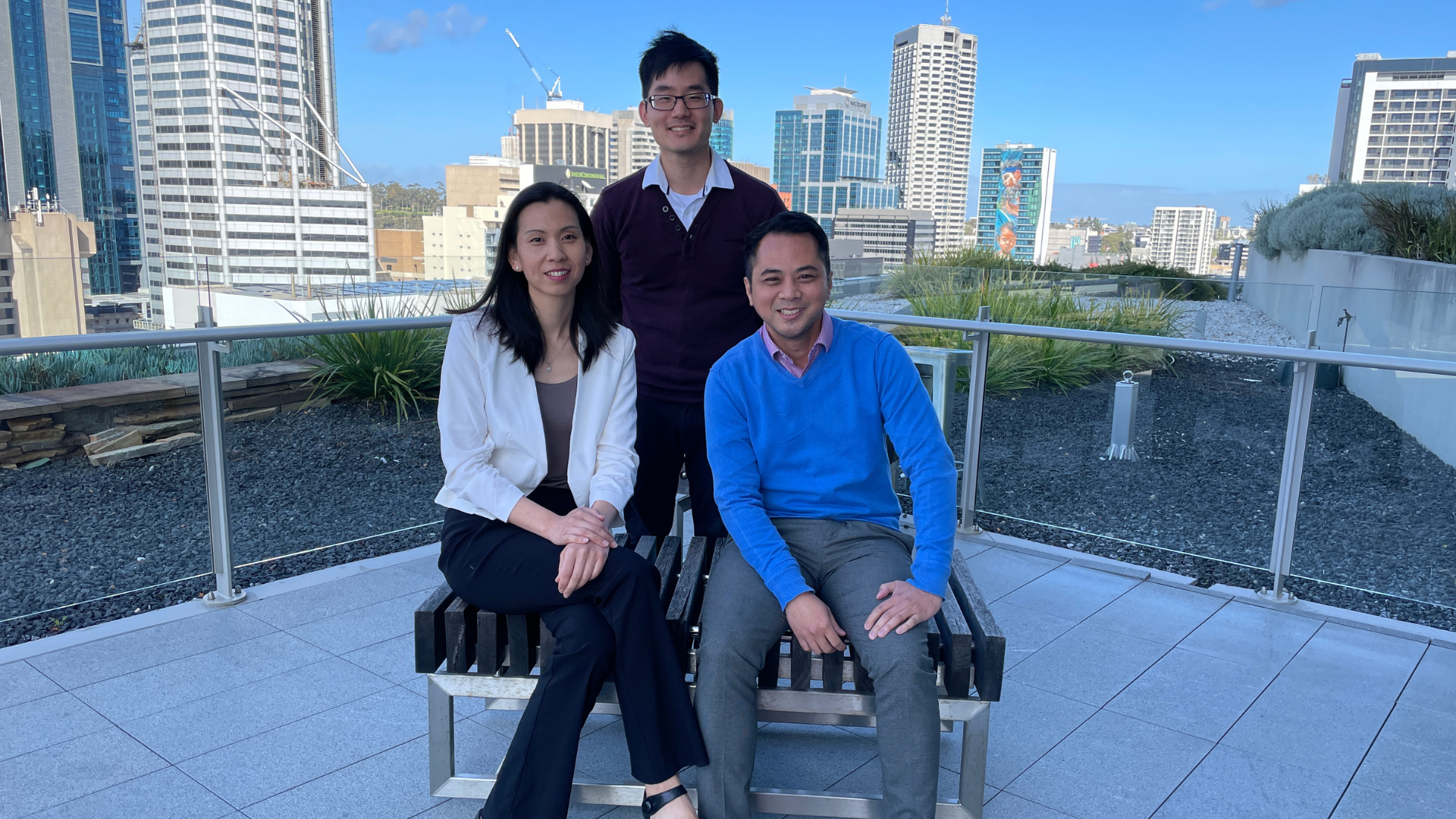 A man and a woman sitting on a bench with a man standing behind them smiling for a photo