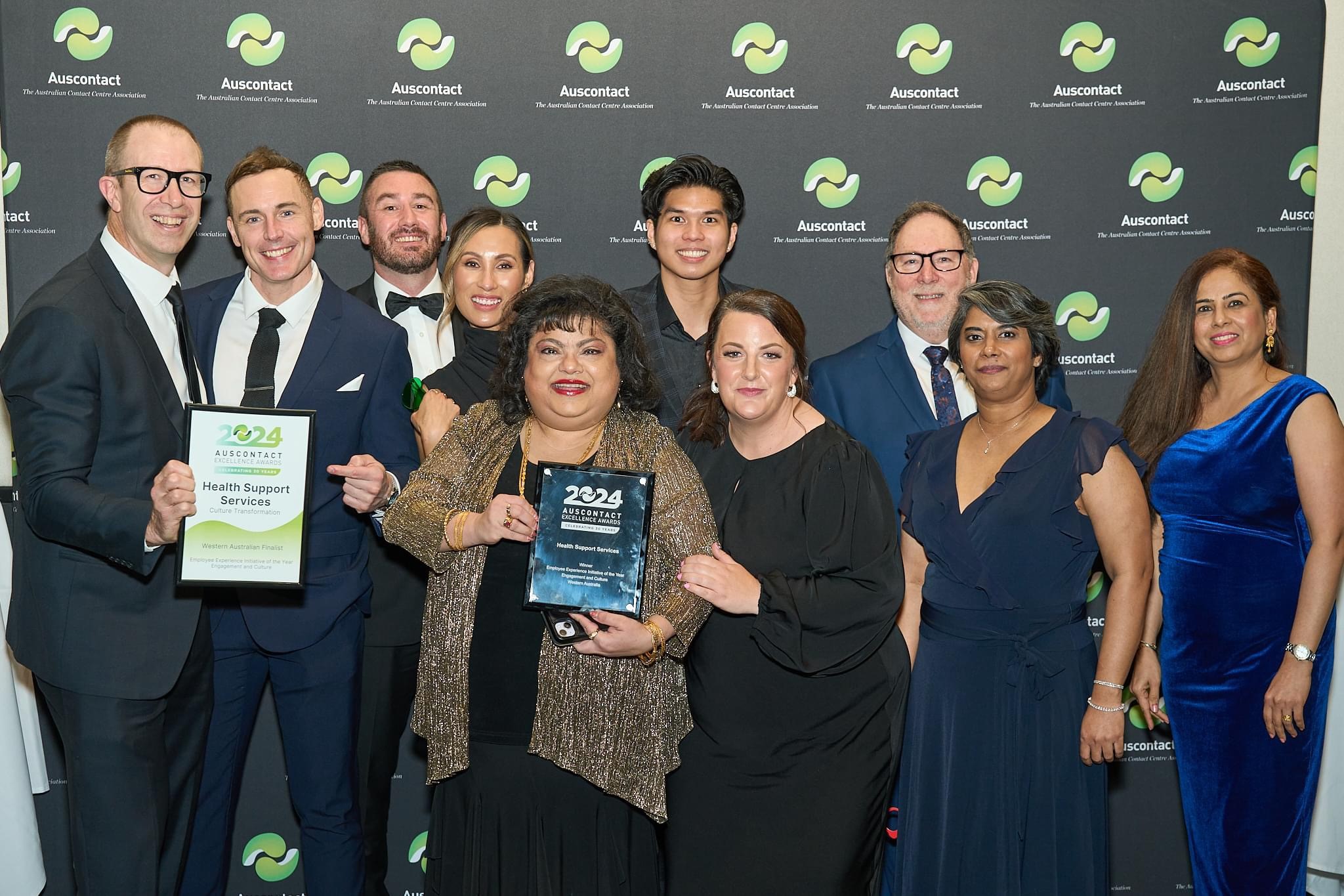 Group of people smiling at the camera, with two people holding a framed certificate