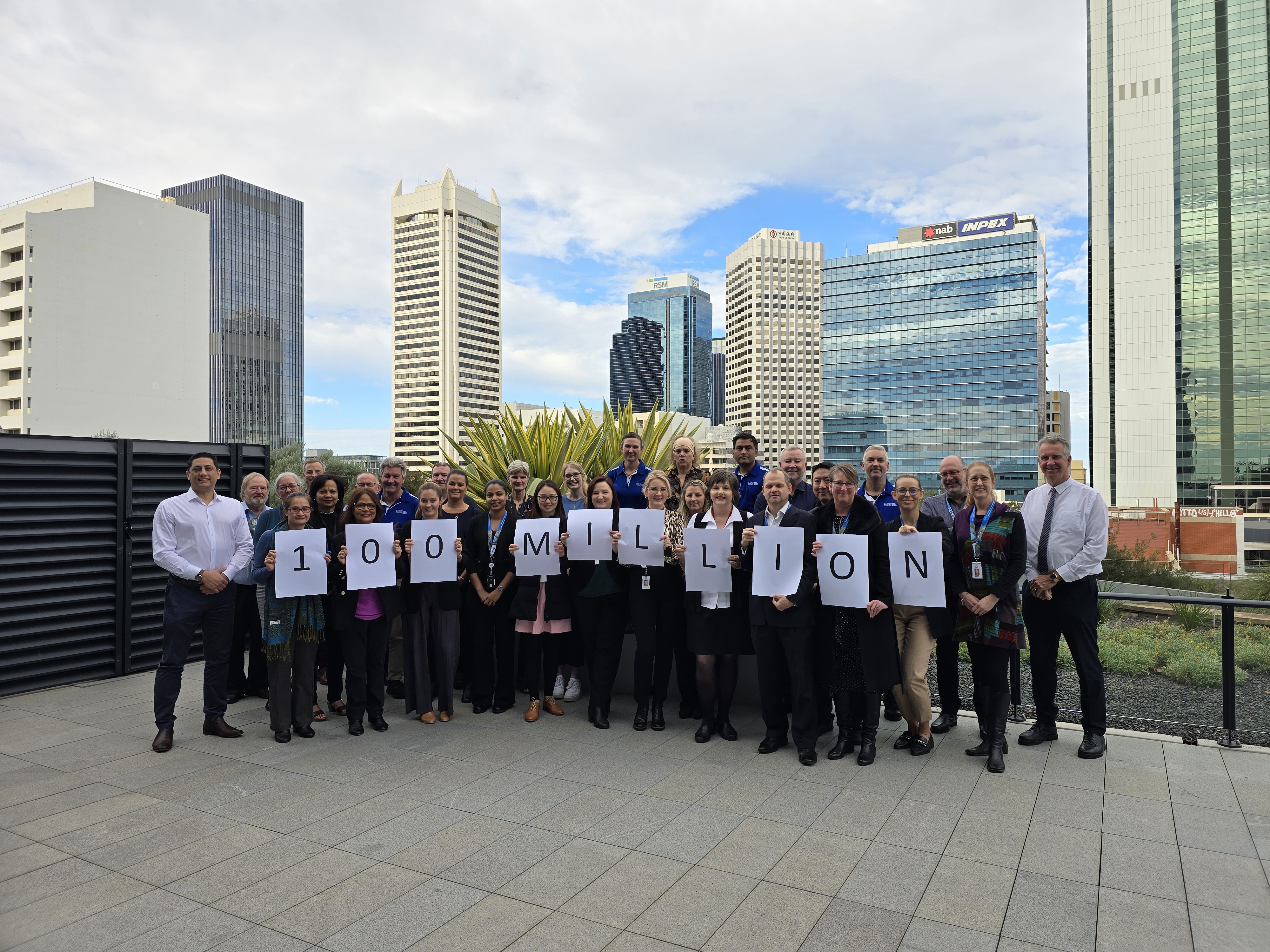 Group of people smiling for the camera, holding single sheets of paper that reads out 100 million